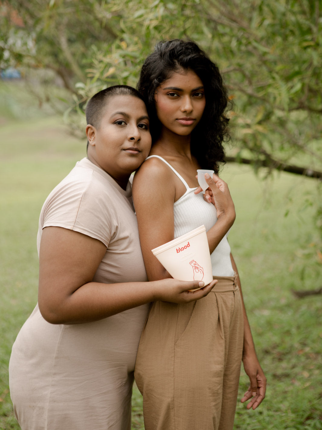 2 girls in a field holding a menstrual cup and sanitising pouch